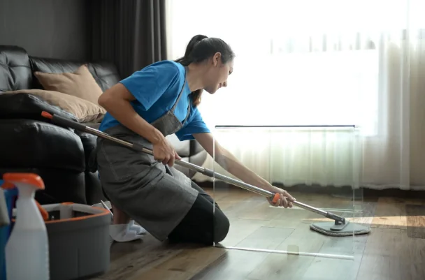 A maid kneeling on the floor of a living room while mopping