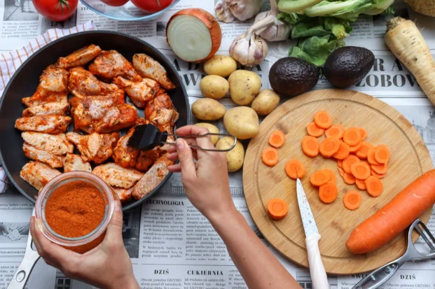 A pan of roasted chicken being prepared in the kitchen alongside some vegetables